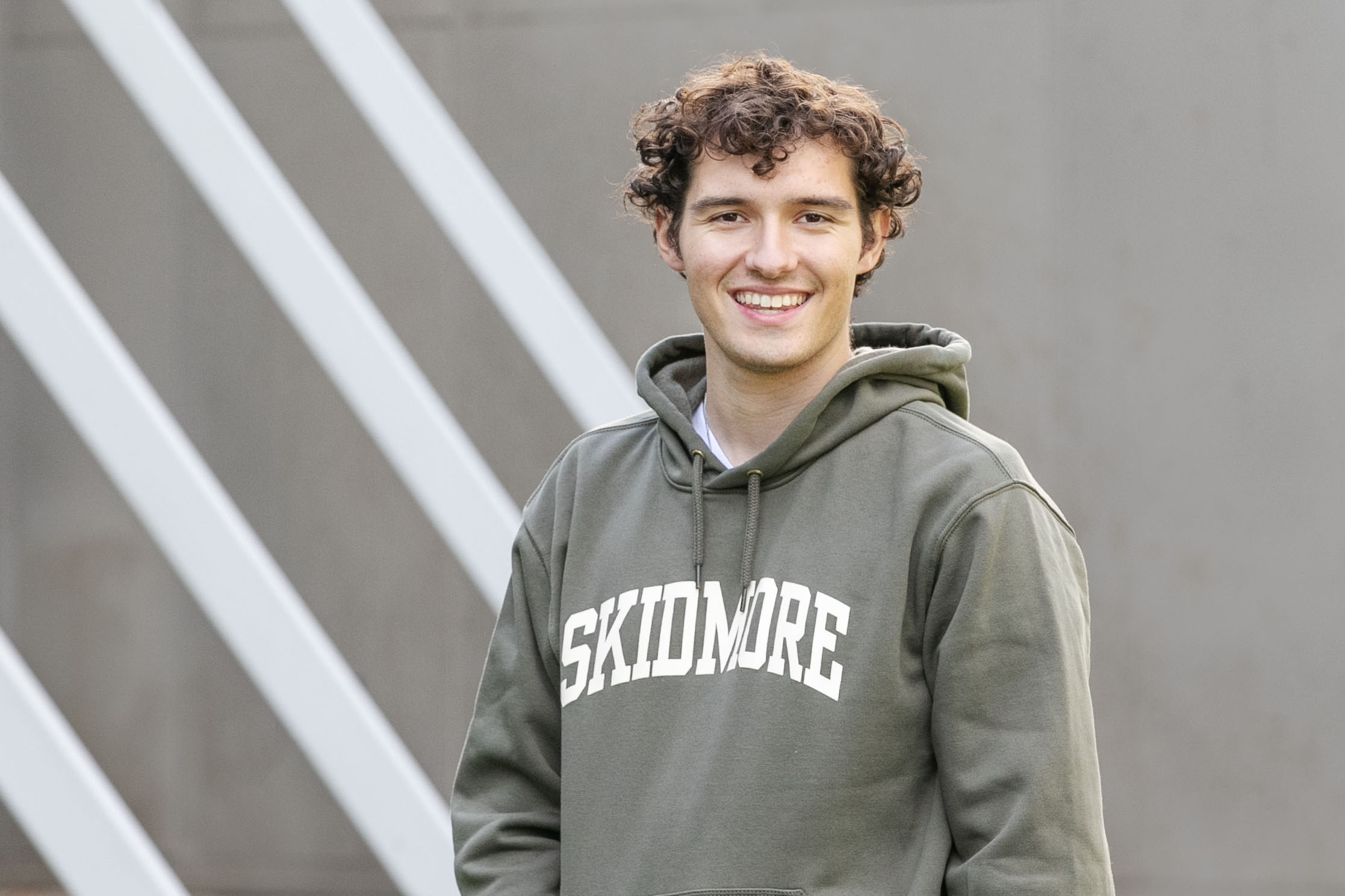 Braedon Quinlan 鈥�24 smiles at the camera while wearing a Skidmore sweatshirt in front of the Tang Teaching Museum.