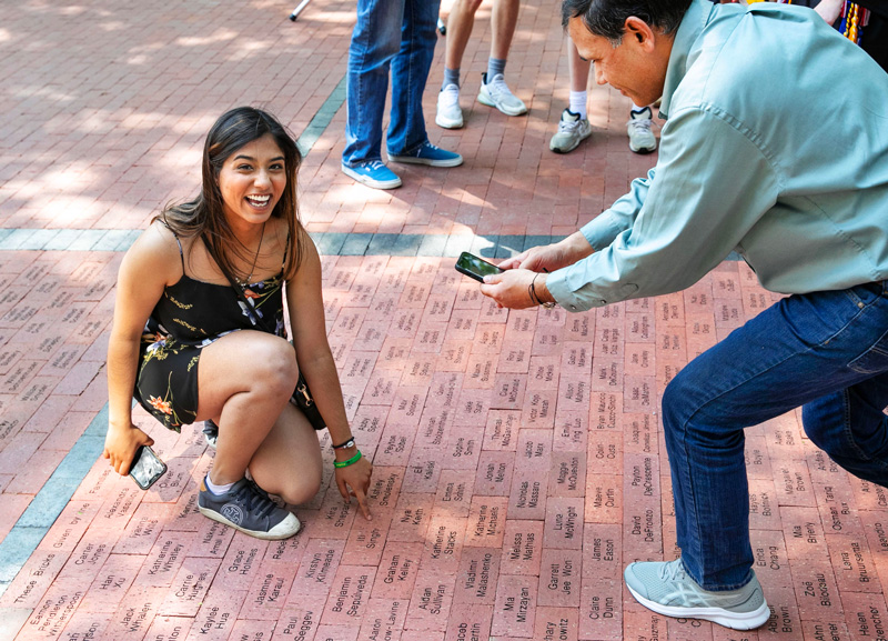 student points to a brick that has their named engraved on a walkway